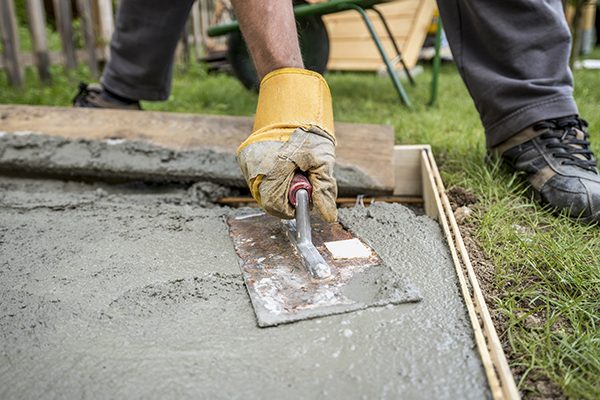 Close up on worker paving or smoothing fresh concrete in plywood walls to be used for an outdoor patio, driveway or sidewalk.